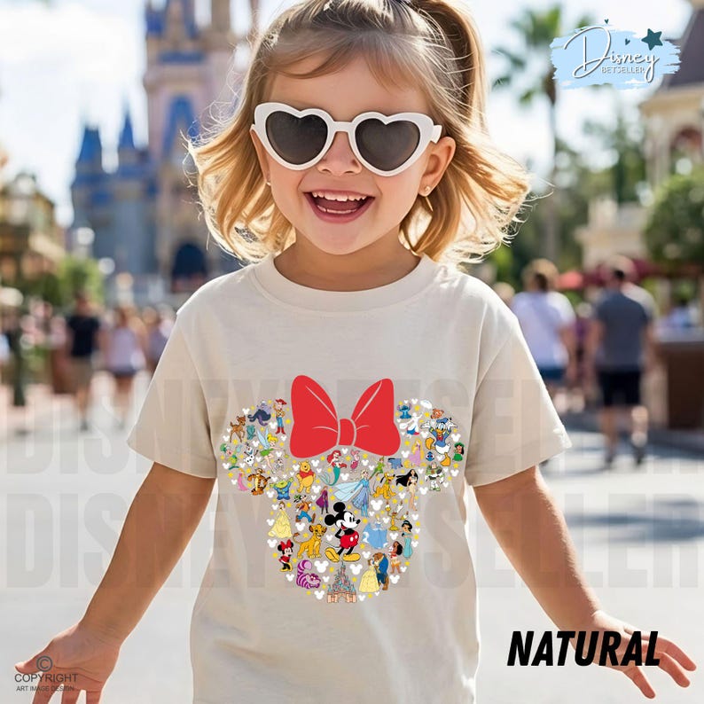 May include: A child wearing a cream-colored t-shirt featuring a Minnie Mouse design. The design includes a red bow and a collage of Disney characters. The word "NATURAL" is printed in black on the bottom right of the shirt.