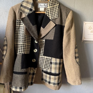 Peut inclure: Un blazer à manches longues avec un motif patchwork composé de tissus beige uni, noir uni et à carreaux noir et blanc. La veste présente un col à revers, quatre boutons sur le devant, deux poches inférieures et des coudières. Étiquette Pati-Pat.