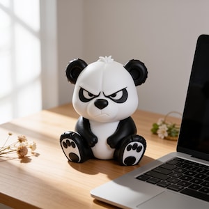 Könnte beinhalten: Eine kleine sitzende Panda-Figur mit weißem Gesicht und Torso sowie schwarzen Ohren, Armen, Beinen und Augenpartien. Der Panda hat einen strengen, finsteren Gesichtsausdruck mit zusammengezogenen Augenbrauen und einer schwarzen Nase.