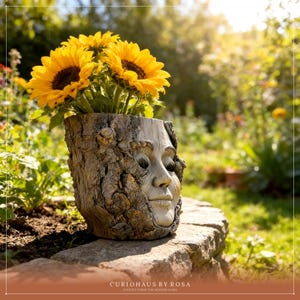 Op de afbeelding: Een unieke, handgemaakte bloempot met een gebeeldhouwd gezicht. De bloempot is gemaakt van een boomstam en gevuld met heldergele zonnebloemen. De bloempot staat op een stenen muur in een tuin.