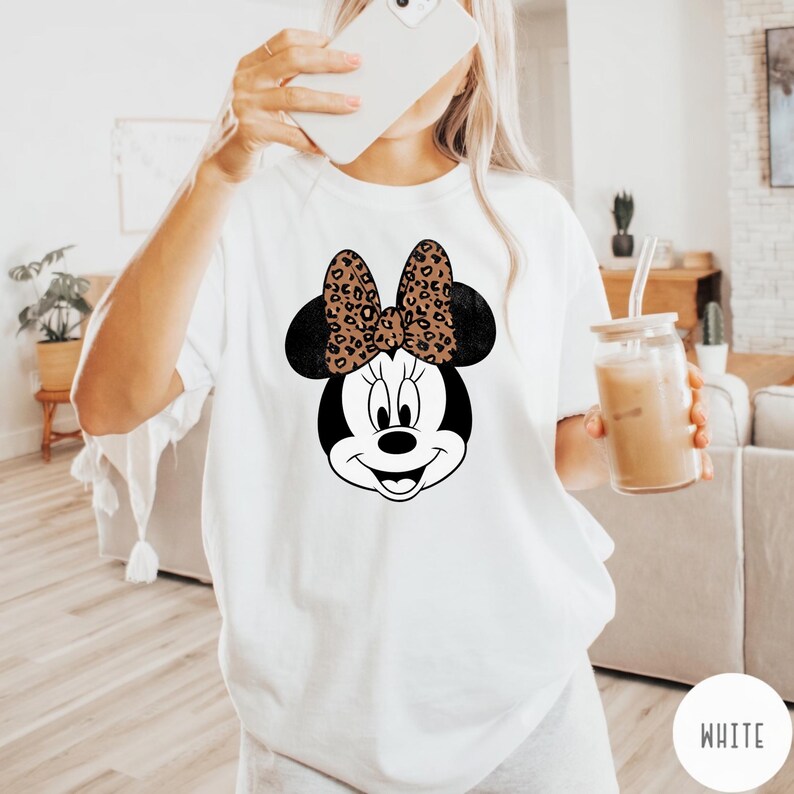 Leopard print Minnie Mouse head with sparkling galaxy-style black ears and a cheetah print bow, Disney-inspired graphic design on a transparent background. Cute Disney vacation shirt design for women, girls, and matching family trip tees
