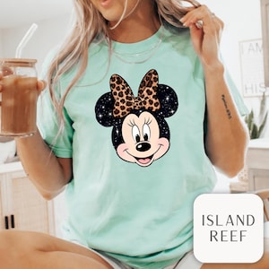 Leopard print Minnie Mouse head with sparkling galaxy-style black ears and a cheetah print bow, Disney-inspired graphic design on a transparent background. Cute Disney vacation shirt design for women, girls, and matching family trip tees