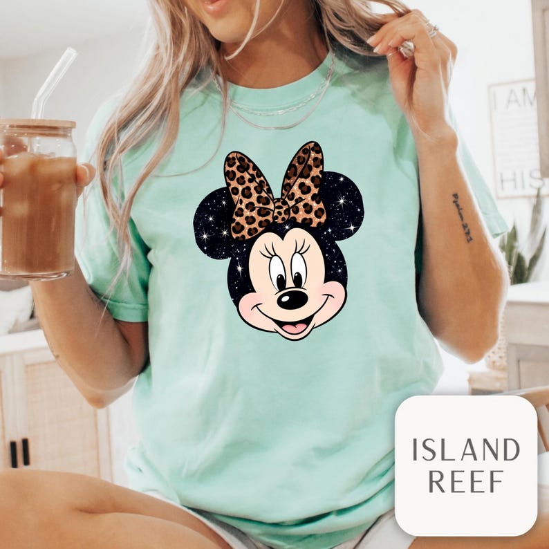 Leopard print Minnie Mouse head with sparkling galaxy-style black ears and a cheetah print bow, Disney-inspired graphic design on a transparent background. Cute Disney vacation shirt design for women, girls, and matching family trip tees