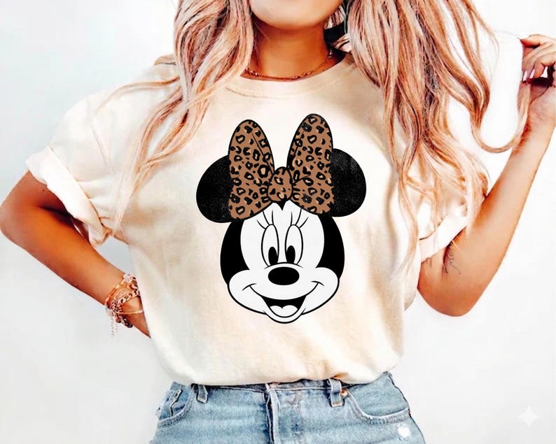 Leopard print Minnie Mouse head with sparkling galaxy-style black ears and a cheetah print bow, Disney-inspired graphic design on a transparent background. Cute Disney vacation shirt design for women, girls, and matching family trip tees