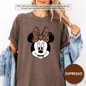 Leopard print Minnie Mouse head with sparkling galaxy-style black ears and a cheetah print bow, Disney-inspired graphic design on a transparent background. Cute Disney vacation shirt design for women, girls, and matching family trip tees