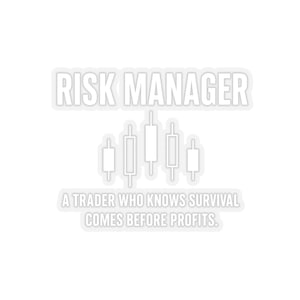 May include: White sticker with the text "RISK MANAGER" in a bold font, above a graphic of candlestick charts. Below, the text reads "A TRADER WHO KNOWS SURVIVAL COMES BEFORE PROFITS."