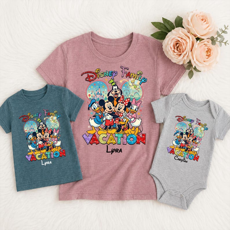 May include: Three Disney-themed shirts and a onesie. The shirts are in teal and mauve, and the onesie is gray. Each garment features a colorful graphic of Disney characters with the text "Disney Family Vacation" and a name. A bouquet of pink roses is in the background.