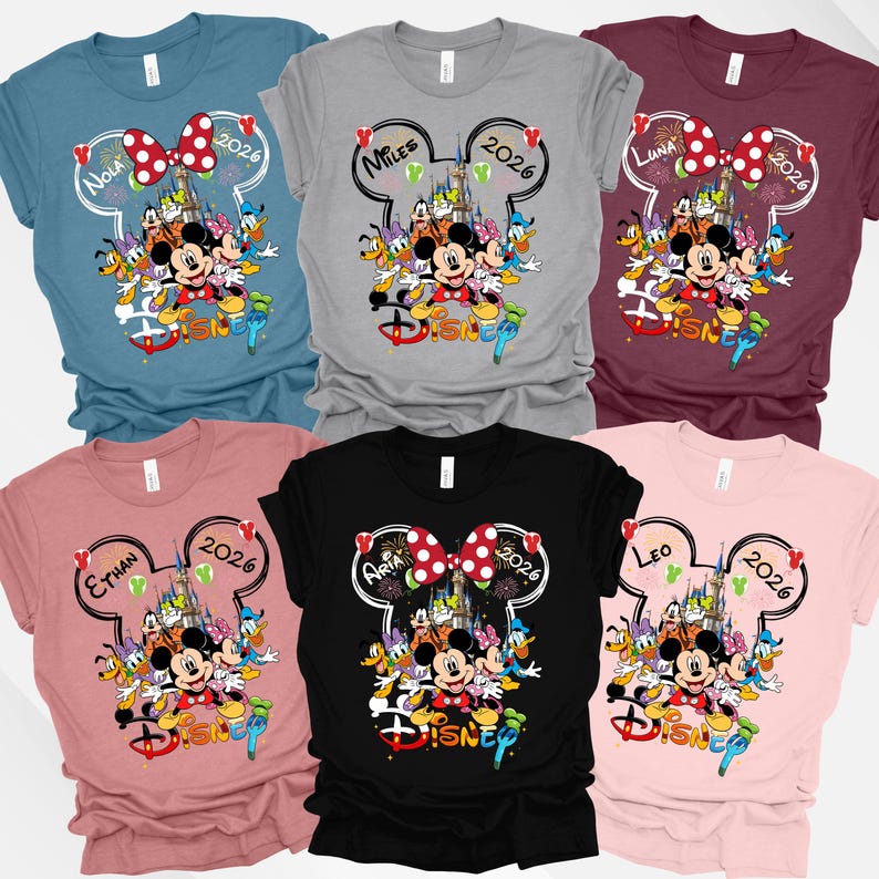 May include: Assorted-color Disney-themed t-shirts. Each shirt features a Mickey Mouse head outline with a name and the year 2026. The shirts display Mickey Mouse, Minnie Mouse, and other Disney characters. The shirts are in various colors.