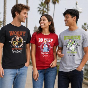 Może przedstawiać: Trzy koszulki z postaciami z Toy Story. Czarna koszulka przedstawia Woody'ego z napisem 'Woody', 'Toy Story', 'Est. 1995' i 'Benjamin'. Czerwona koszulka przedstawia Bo Peep z 'Bo Peep', 'Toy Story', 'Est. 1995' i 'Emma'. Szara koszulka przedstawia Buzza Astrala z 'Buzz Lightyear', 'Toy Story', 'Est. 1995' i 'Lucas'.