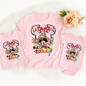 May include: Three pink Disney-themed shirts. The shirts feature a Minnie Mouse bow design with the text "2026" and the names "Zoe" and "Eni". The shirts also have a colorful graphic of Mickey Mouse and friends.