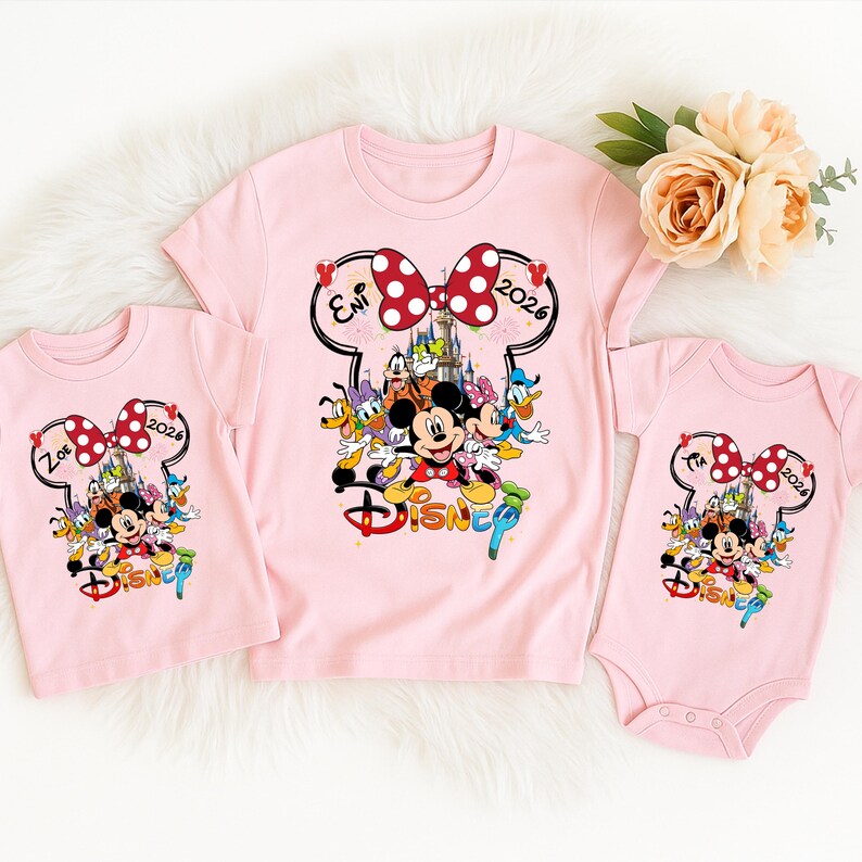 May include: Three pink Disney-themed shirts. The shirts feature a Minnie Mouse bow design with the text "2026" and the names "Zoe" and "Eni". The shirts also have a colorful graphic of Mickey Mouse and friends.