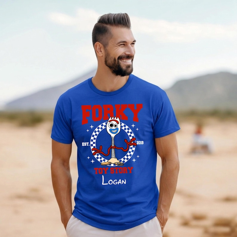 Może przedstawiać: Kr&oacute;lewsko-niebieski t-shirt z grafiką przedstawiającą postać Forky z Toy Story. Wz&oacute;r zawiera czerwony napis FORKY, niebieski tekst TOY STORY oraz białe imię Logan. Postać otoczona jest szachownicowym kołem z napisem EST. 2019.
