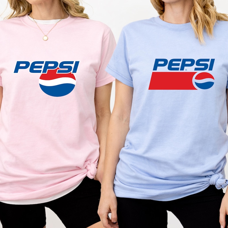 May include: Two short-sleeved t-shirts, one light pink and one light blue, each featuring the Pepsi logo. The logo includes the word "PEPSI" in blue, with a red and blue design. The shirts are a casual style.