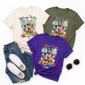 May include: Three t-shirts with a Disney Family Vacation graphic. The shirts are cream, olive green, and purple. The graphic features Mickey Mouse, Minnie Mouse, Donald Duck, and other Disney characters. The purple shirt has the name "Elara" on it. A pair of blue jeans, white sneakers, and sunglasses are also in the image.