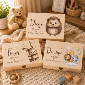 May include: Three rectangular light-colored wooden keepsake boxes featuring personalized names, birth dates, times, weights, and lengths. The boxes display illustrations of a hedgehog, a rabbit on a swing, and a lion, giraffe, and elephant with balloons.