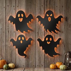 Peut inclure: Quatre décorations murales en forme de fantôme noir avec des yeux et des bouches découpés, rétroéclairées par une lueur orange chaude. Chaque fantôme présente une expression faciale unique, souriante, surprise ou en colère, sur un mur en bois.