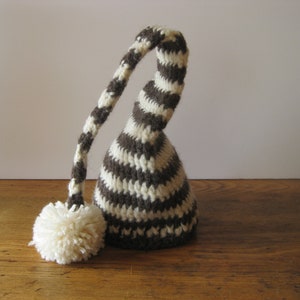May include: A brown and white striped knitted elf hat with a long, curled brim and a white pom-pom.