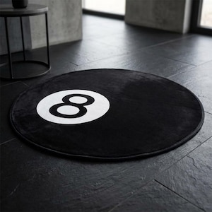 Peut inclure: Tapis rond noir avec un grand chiffre 8 blanc au centre. Le tapis est fait d'une matière douce et est posé sur un sol carrelé sombre. C'est un article de décoration.