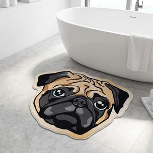 May include: A beige and black pug-shaped bath mat. The mat features a detailed illustration of a pug's face, with black eyes, a black nose, and a beige and brown coat. The mat is placed on a tiled floor near a white bathtub.
