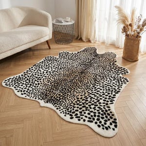 Puede incluir: Una alfombra de imitación piel de vaca con fondo blanco y manchas negras. La alfombra, con forma de piel de vaca, está colocada sobre un suelo de madera. Es un elemento decorativo para salón o dormitorio.