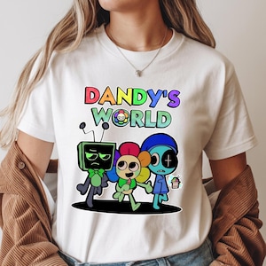 May include: White t-shirt with the text "DANDY'S WORLD" in rainbow-coloured letters. The design includes three cartoon characters: a green TV-headed figure, a flower-headed figure, and a blue-skinned figure.