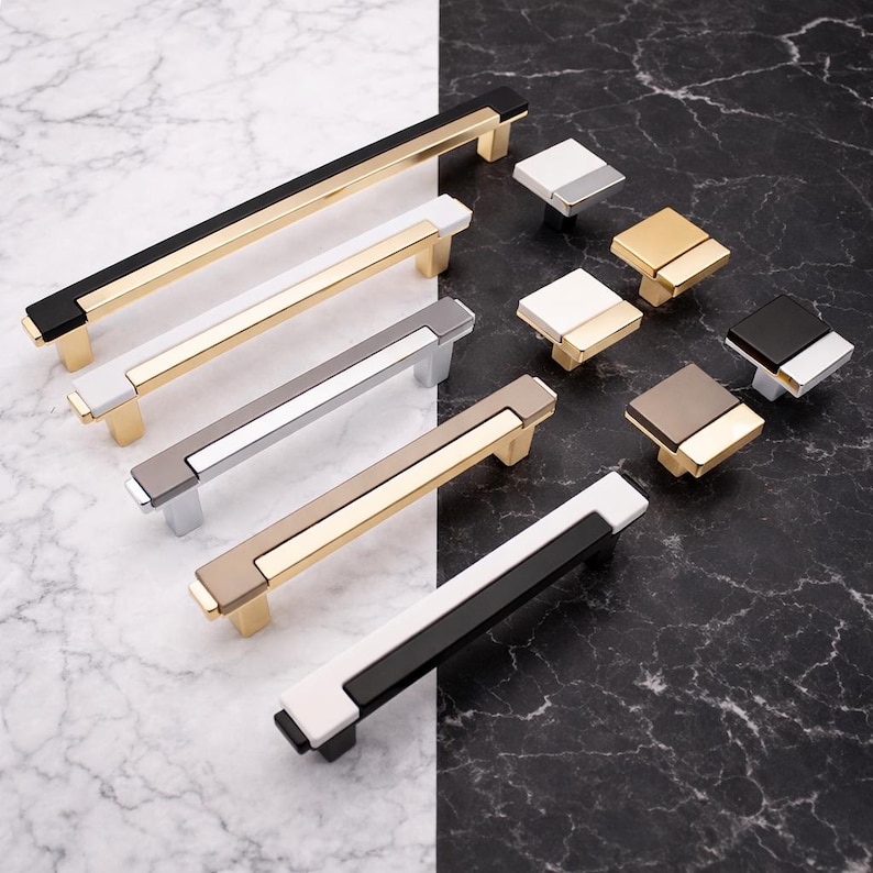 Peut inclure: Une collection de quincaillerie de meubles moderne, comprenant des barres de tirage et des boutons carr&eacute;s. Les poign&eacute;es ont un design rectangulaire avec des accents dor&eacute;s, noirs, blancs, argent&eacute;s et taupe. Les boutons sont carr&eacute;s avec des couleurs similaires.