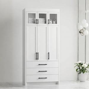 May include: A tall, white bathroom cabinet with black hardware. The cabinet has three drawers, three solid doors, and three glass-paned doors at the top. Inside the glass doors are folded white towels and toiletries. The cabinet is set against a white wall.