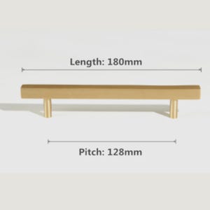 Pode incluir: Um puxador de m&oacute;vel dourado com uma barra retangular e dois suportes de montagem cil&iacute;ndricos. O puxador tem um comprimento total de 180 mm e uma dist&acirc;ncia entre furos de 128 mm, conforme indicado pelas etiquetas de texto na imagem.