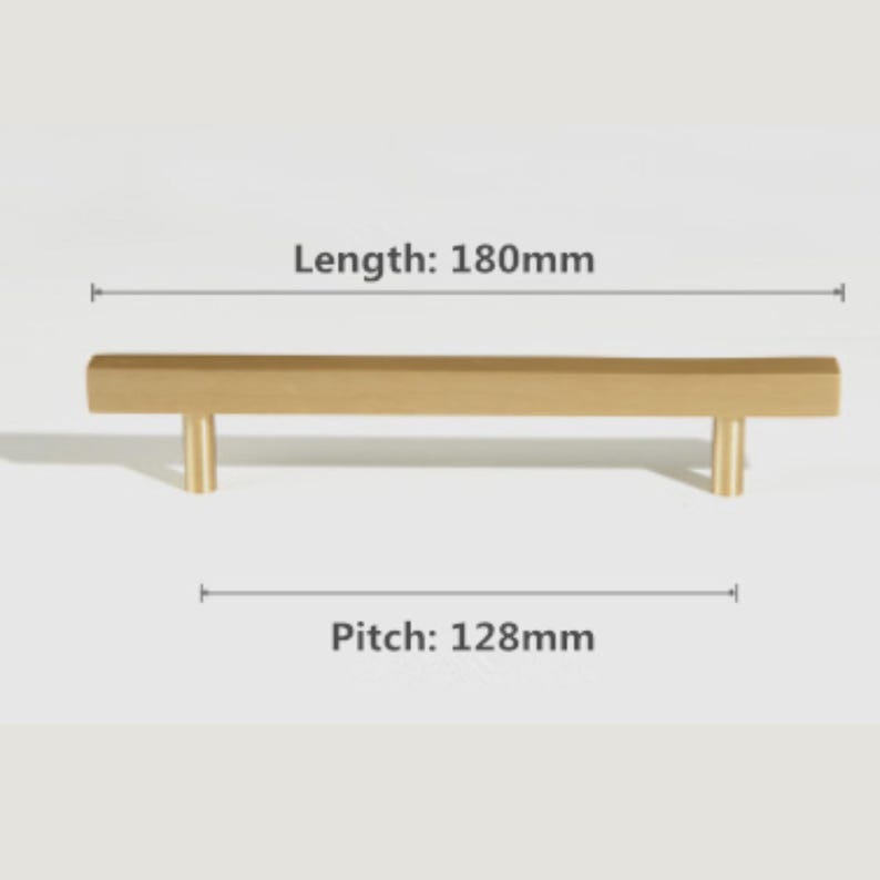 Pode incluir: Um puxador de m&oacute;vel dourado com uma barra retangular e dois suportes de montagem cil&iacute;ndricos. O puxador tem um comprimento total de 180 mm e uma dist&acirc;ncia entre furos de 128 mm, conforme indicado pelas etiquetas de texto na imagem.