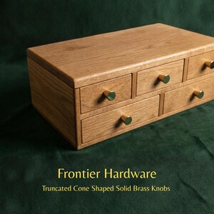 May include: A rectangular wooden storage chest featuring five drawers of varying sizes, each fitted with a small, truncated cone-shaped solid brass knob. The text Frontier Hardware Truncated Cone Shaped Solid Brass Knobs is visible below.