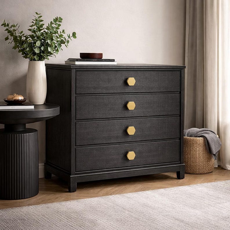 May include: A dark charcoal gray wooden dresser featuring four horizontal drawers, each equipped with a single hexagonal gold-toned knob. The dresser has a rectangular frame with a flat top surface and stands on four short, sturdy block feet.