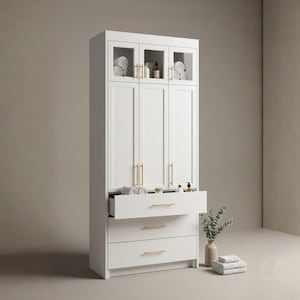 May include: A white bathroom cabinet with three doors and three drawers. The top section has glass-fronted doors, displaying rolled towels and toiletries. Gold-colored handles adorn the doors and drawers. A drawer is partially open, revealing towels and accessories.