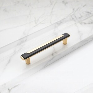 Peut inclure: Poign&eacute;e de meuble rectangulaire avec une section centrale noire, un accent dor&eacute; et des montants dor&eacute;s. Cette poign&eacute;e est con&ccedil;ue pour les tiroirs et les armoires. Mesure environ 15 cm de long.
