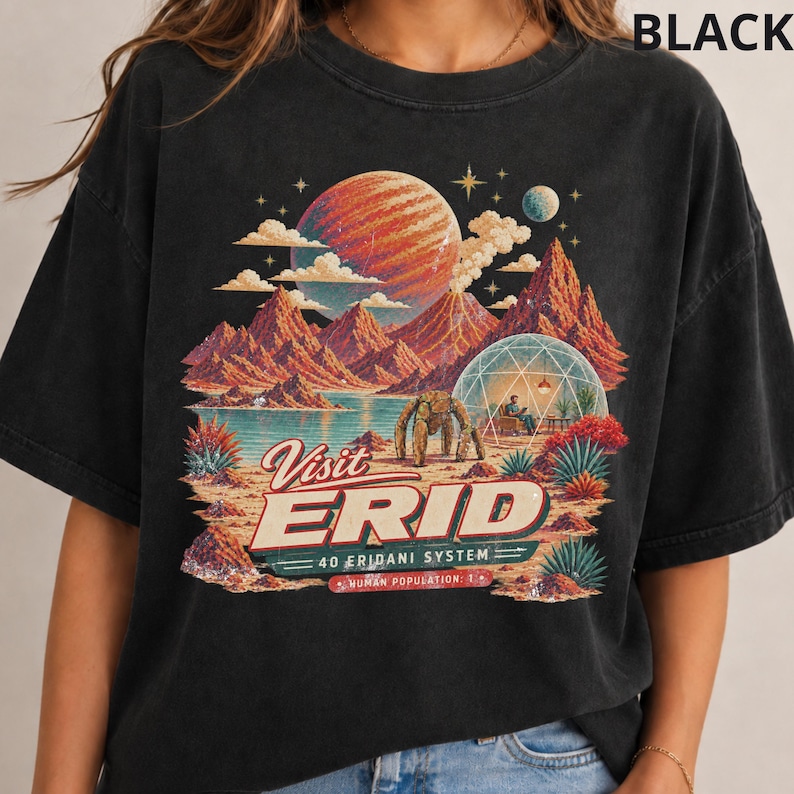 May include: A black t-shirt featuring a graphic print of a space landscape with a large planet, mountains, a geodesic dome, and a robotic figure. The text reads Visit ERID 40 ERIDANI SYSTEM HUMAN POPULATION: 1. The design uses orange, blue, and green tones.