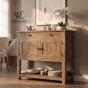 May include: A wooden sideboard featuring two top drawers and two lower cabinet doors with dark metal knobs. The piece includes an open bottom shelf holding a ceramic bowl, candles, and woven mats. The logo Woodlino Handmade Wooden Creations is visible.