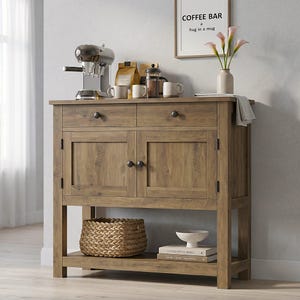 May include: A wooden coffee bar cabinet with two drawers and two doors. It features a lower shelf with a woven basket and decorative items. A coffee maker, mugs, and a framed sign that says "Coffee Bar, a hug in a mug" are on top.