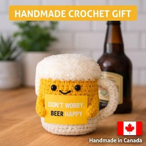 May include: Handmade crochet beer mug with a smiling face and the text "DON'T WORRY, BEER HAPPY." The mug is yellow with white "foam" and a white handle. A brown beer bottle is in the background. The text "HANDMADE CROCHET GIFT" is at the top.