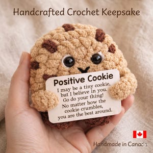 May include: Handmade crochet cookie keepsake with chocolate chip details. The cookie holds a sign that reads "Positive Cookie" with an inspirational message. The item is handmade in Canada.