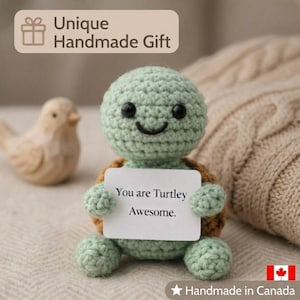 Pode incluir: Uma tartaruga de crochê feita à mão com cabeça e membros verdes, casco marrom e olhos pretos. A tartaruga segura uma placa que diz "You are Turtley Awesome". A imagem também inclui o texto "Unique Handmade Gift."