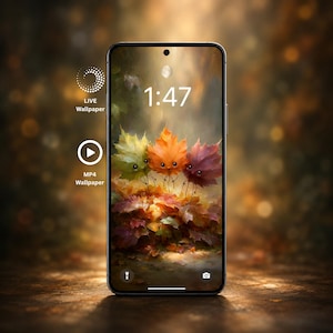 Könnte beinhalten: Ein Smartphone mit einem digitalen Hintergrundbild von drei kleinen, animierten Herbstblättern mit Gesichtern auf einem Haufen Laub. Der Bildschirm zeigt die Uhrzeit 1:47, ein Taschenlampensymbol, ein Kamerasymbol sowie den Text LIVE Wallpaper und MP4 Wallpaper.