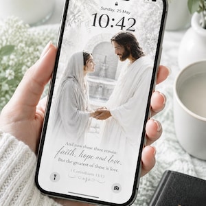 以下が含まれることがあります： スマートフォンには、手をつないでいる2人の人物の宗教的な画像が表示され、「信仰、希望、愛」というテキストが表示されています。 金色の文字と十字架が付いた黒い聖書が見えます。 電話には日付と時刻が表示されます。