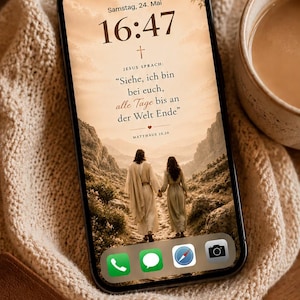 Könnte beinhalten: Ein Smartphone mit einem Hintergrundbild von zwei Personen, die einen Bergpfad hinaufgehen, mit dem Text "Jesus sprach: Siehe, ich bin bei euch, alle Tage bis an der Welt Ende." Eine Bibel und eine Kaffeetasse liegen daneben.