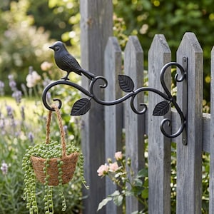 May include: A black metal bird and leaf design hanging basket bracket attached to a wooden fence. A woven basket filled with green plants hangs from the bracket. The bracket is a decorative garden accent.