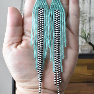 May include: A pair of long, beaded earrings with a turquoise and black and white geometric pattern.