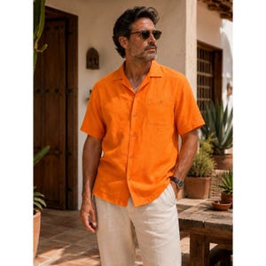 May include: A short-sleeved, bright orange button-down shirt with a classic collar and a single chest pocket, paired with light beige trousers. The shirt features a textured fabric finish and is worn with dark-tinted sunglasses and a wristwatch.