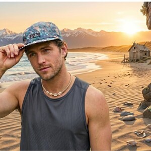 Puede incluir: Una gorra de cinco paneles con fondo verde azulado oscuro y un patrón de hojas de palmera tropical en tonos verdes, azules y blancos, acompañada de un collar sencillo hecho de pequeñas conchas naturales claras en un cordón.