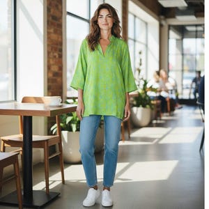 May include: A bright lime green tunic with a subtle blue paisley pattern, featuring three-quarter length sleeves and a split neckline, paired with light blue denim jeans and clean white sneakers. The outfit is casual and features a loose fit.