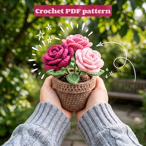 Puede incluir: Un patrón de crochet en PDF que presenta tres rosas de hilo hechas a mano en tonos magenta oscuro, rosa medio y rosa claro, plantadas en una maceta de crochet marrón con hojas verdes. El texto "Crochet PDF pattern" aparece en la parte superior.