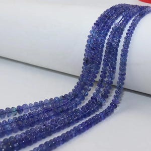 May include: Multiple strands of small, faceted, round tanzanite beads in a deep violet-blue hue. The beads are strung together on thin thread, creating a uniform, shimmering appearance with consistent color saturation throughout each individual strand.