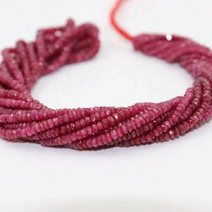 May include: A strand of small, faceted, deep pinkish-red gemstone beads arranged in a circular shape. The beads are strung on a thin red cord, showcasing a uniform, circular cut with a reflective, textured surface across the entire collection.